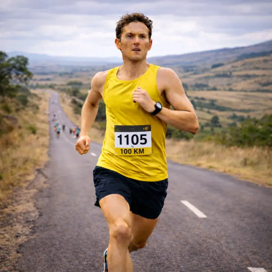 Ultra-distance runner competing on a long rural road with distant runners behind during a 100 km running training plan