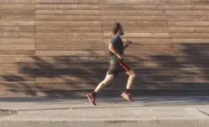 Runner striding along a paved footpath with midfoot strike, demonstrating proper running cadence technique