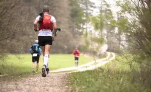 Trail runner with backpack jogging through a forest trail during early morning run