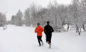 Two runners wearing winter running gear running through snow-covered trail