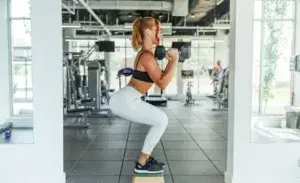 Gym exercises for runners – woman performing a weighted box squat for strength and balance.
