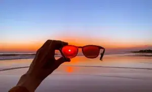Person holding running sunglasses during sunset on the beach