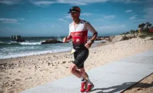 Triathlete running along beach wearing a red and white tri suit during a race.