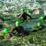 Half Ironman swim distance open water triathletes wearing wetsuits and green swim caps.