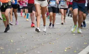 Runners pushing towards the finish line during a sub 2 hour half marathon event, with legs in motion and race bibs visible on the street covered in confetti.