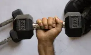 Close-up of a hand holding two 5KG dumbbells for 10 dumbbell exercises to build upper chest