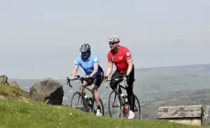 Two cyclists riding uphill through rolling countryside during an elevation gain cycling training ride.