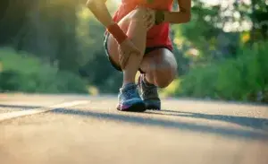 How to run with shin splints — runner crouching on road holding lower leg in pain.