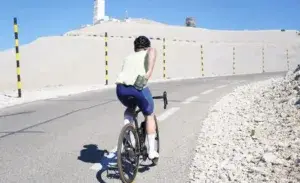 Cyclist climbing a mountain road while adjusting saddle position — how to treat cycling saddle sores during long rides.