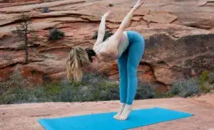 A woman performs a balance-focused stretch on a yoga mat in a scenic desert setting, demonstrating one of the many effective mobility exercises for runners that improve flexibility, control, and posture before a run.