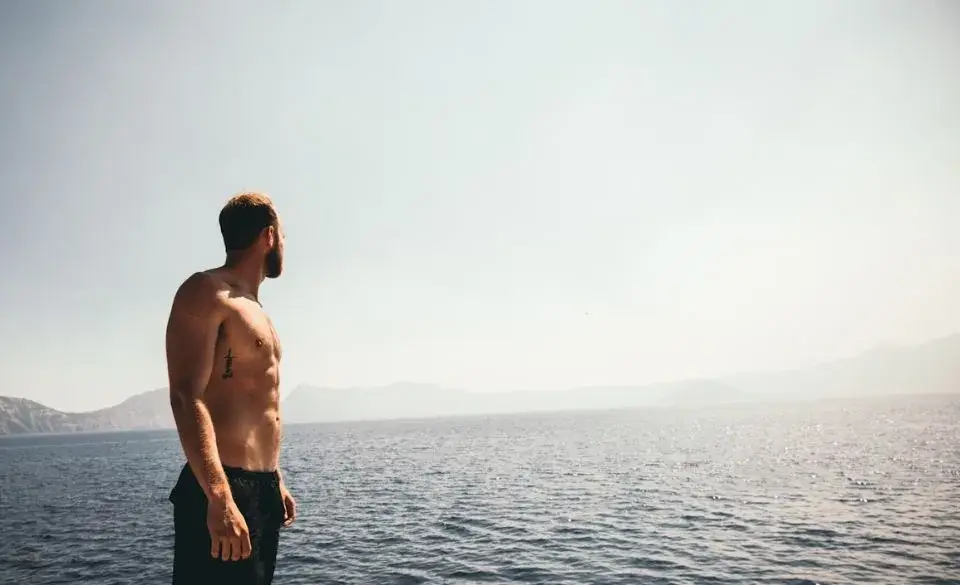 Fit man with visible abs from running standing by the ocean.