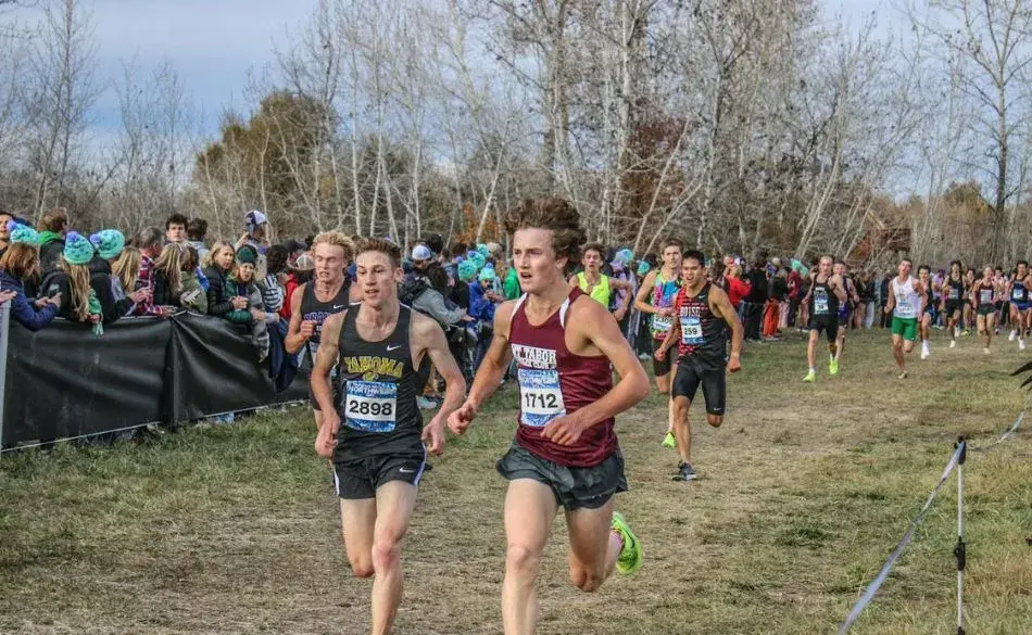 High school athletes competing in a cross country race with spectators cheering from the sidelines