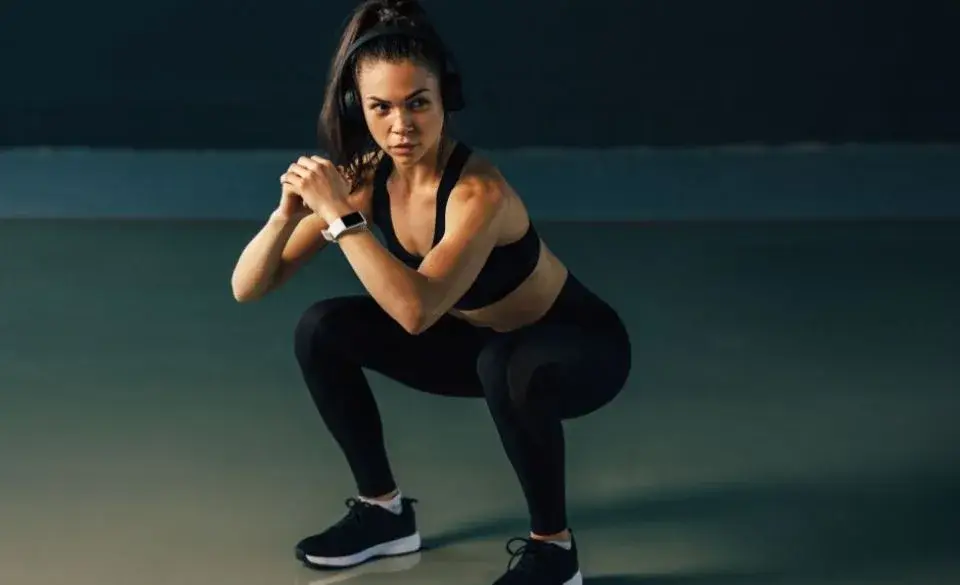 Woman performing duck walk exercise in deep squat position to strengthen legs and improve mobility.