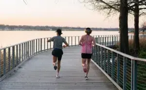 Two runners pacing together along a lakeside boardwalk at sunrise, learning how to calculate pace for running