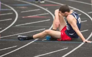 Runner sitting on a track experiencing leg pain, illustrating how to avoid cramps while running