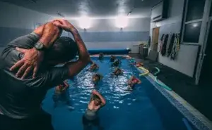A group of athletes performing non weight bearing exercises for runners in a pool, guided by a coach leading warm-up stretches before aqua jogging.