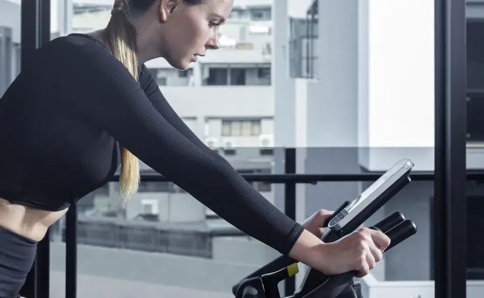 Treadmill vs bike indoor workout woman cycling on stationary bike.