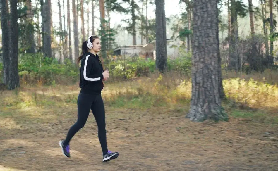 Woman practicing walking exercise routines in the forest while listening to music