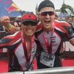 Triathletes celebrating at an Ironman finish line after completing their race, representing the SportCoaching community and professional triathlon coaching success in Australia