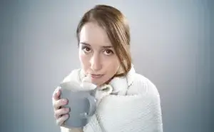 woman wrapped in a blanket holding a mug while sick illustrating running with a cold