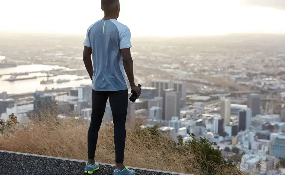 Runner standing on a hill overlooking the city at sunrise, preparing for hill workouts for marathon training