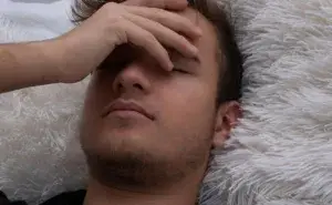 Man lying down with a headache, representing the question: is it safe to run with a fever.