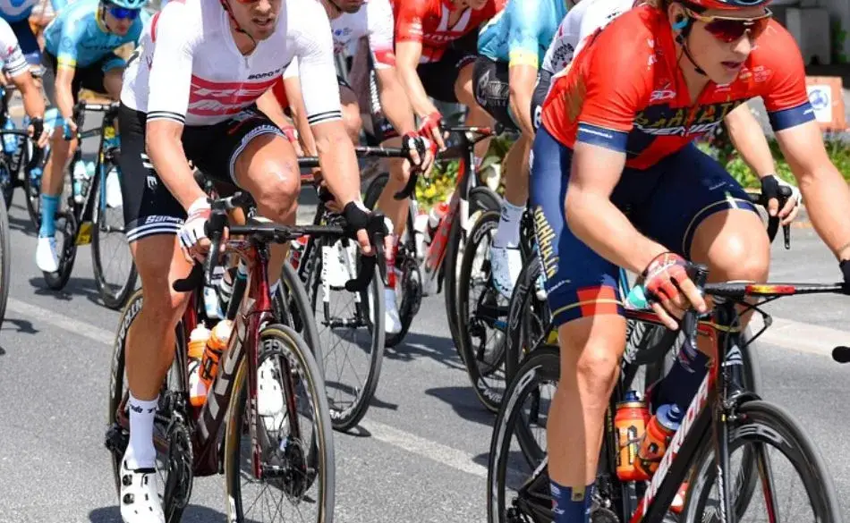 Cyclists riding in a fast-paced group during a road race showing the effort that can make riders ask why do my quads burn when cycling