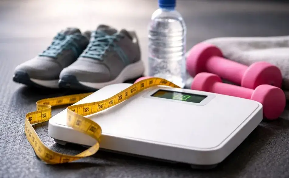 Exercising but putting on weight shown by bathroom scale, running shoes, dumbbells, and tape measure after training