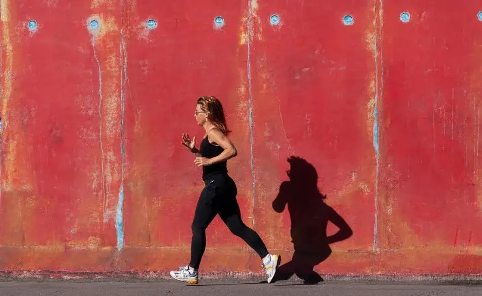 Runner moving along a red wall with visible stride pattern showing signs of favoring a leg while running.