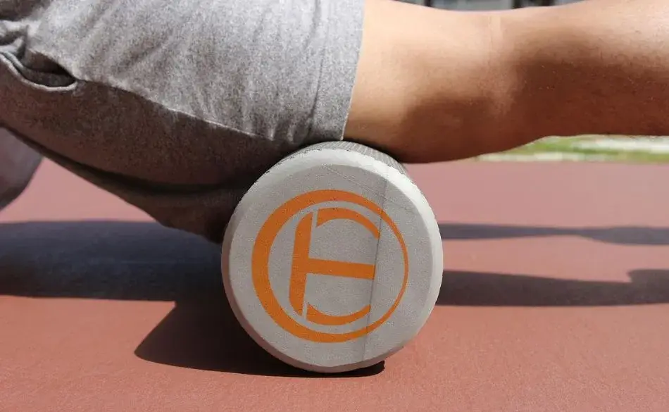 Person using a foam roller under their hamstring during recovery on an outdoor track.