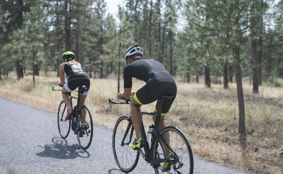 Cyclists training on a quiet forest road during an Ironman 70.3 preparation period, showing how long it takes to train for an Ironman 70.3