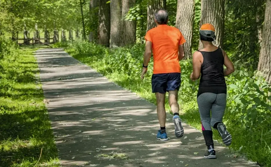 Two beginner runners jogging together on a tree-lined path during a Couch to 5K training session