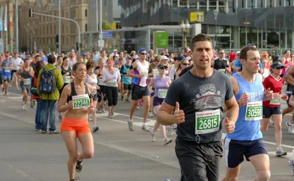 Runners racing through a city street during the Melbourne half marathon event with race bibs and crowd support