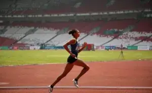 Female track athlete running on a red athletics track in a large stadium, demonstrating good running form with arms bent and forward lean