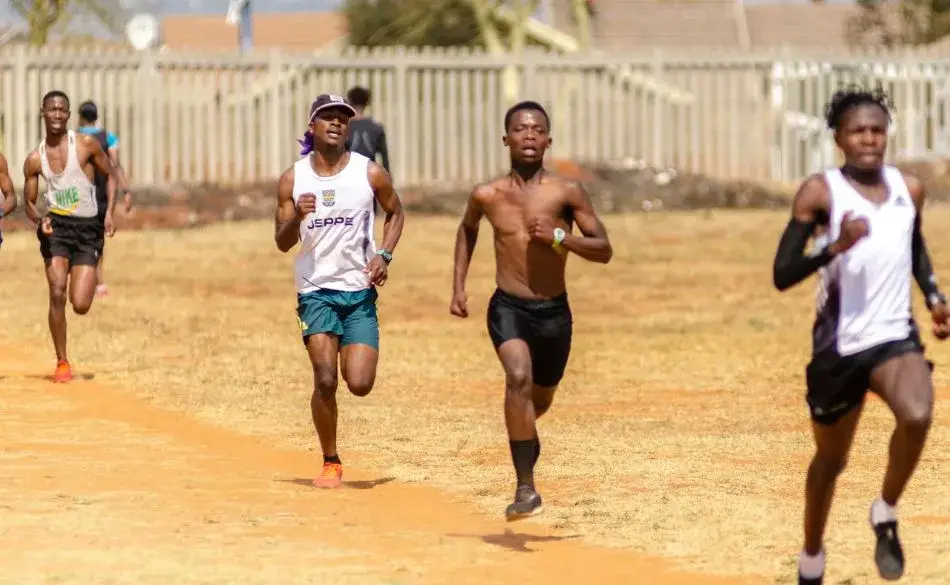 Runners demonstrating high cadence and upright posture during a cross-country race on a dirt track