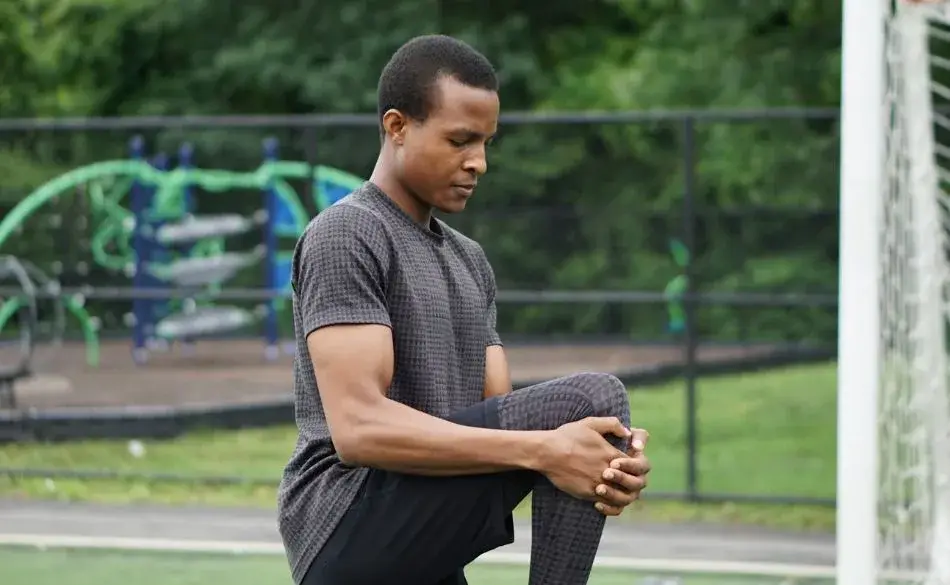 Runner performing a standing knee-to-chest stretch as part of a dynamic warm-up routine