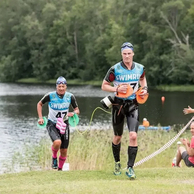 Two swimrun athletes exiting the water and running towards the transition area.